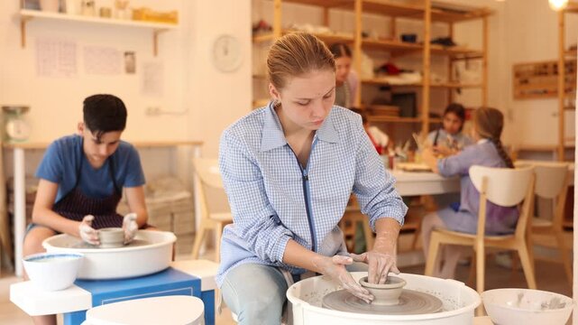 Pleased underage attendees of pottery circle working at throwing-wheel with female instructor