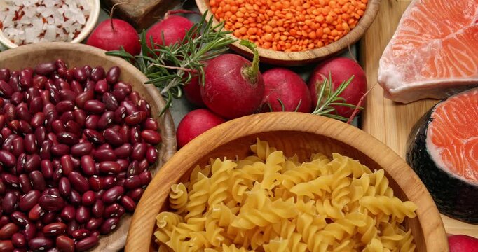 Healthy products on a gray table. Close-up footage of fish, meat, chicken, onion, radish, lettuce, mint, avocado, tomatoes, potatoes, eggs, rice, carrots, lentils, macaroni, corn porridge.