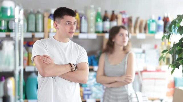 Spouses yell at each other in sales area of household store. Angry and stubborn guy and girl are indignant and swear, family conflict. Couple is arguing and yell at each other