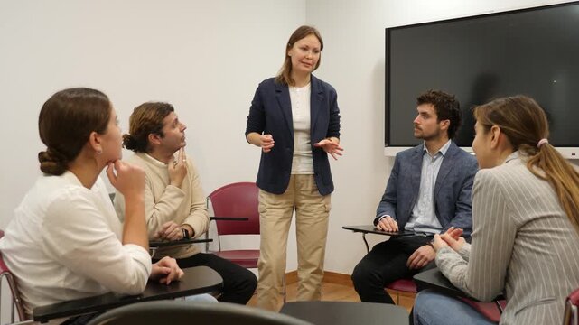  Friendly businesswoman standing near interactive board and communicating with group of adult students at seminar in advanced training