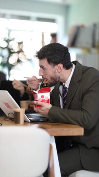 Lunch break in office, mam employee eating Chinese noodles with chopsticks, food with delivery. Staff use break time for lunch and rest