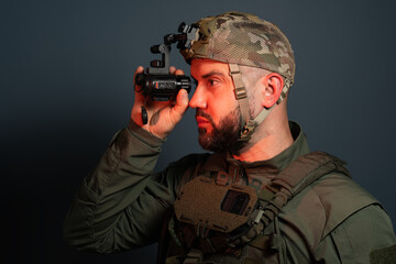 Studio profile portrait of a tactical military soldier wearing a night vision cap while adjusting diopter settings on a helmet-mounted thermal monocular © Dmitri