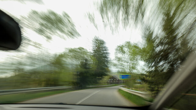 Blurry view from car window on a winding road through green trees