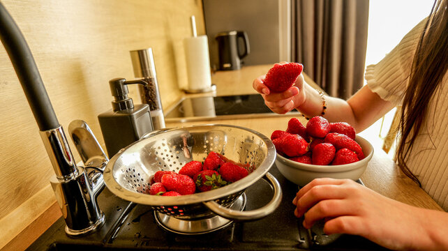 Woman washing fresh strawberries in a kitchen sink with a colander