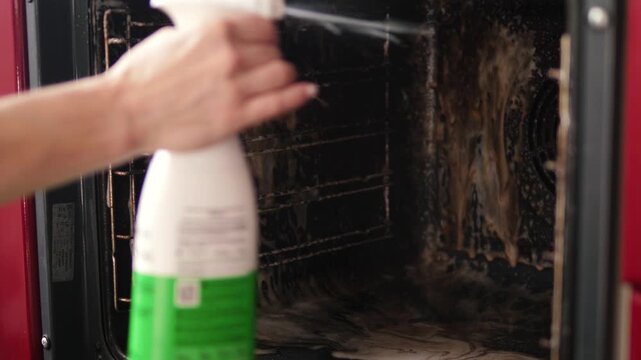 A woman sprays cleaner into a very dirty oven. This is a detailed process of cleaning the kitchen and fighting heavy grease buildup