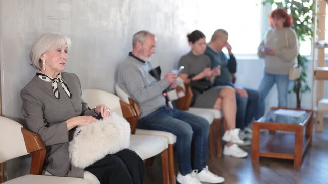 Group of elderly people sitting in chairs in queue to see doctor in lobby big medical facility