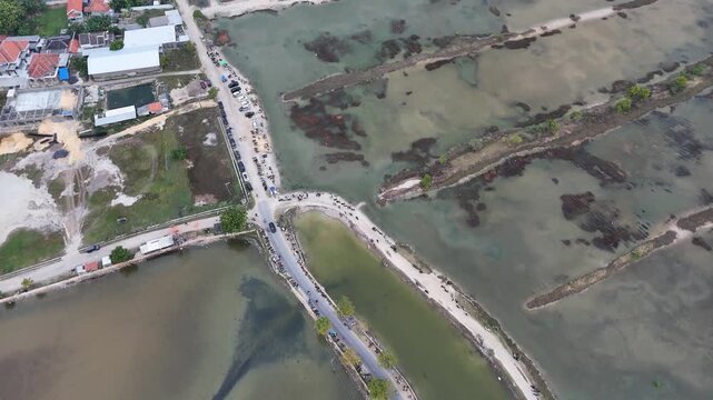 Aerial view of a coastal road crossing fishponds and village settlement in Indonesia