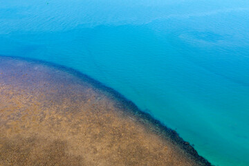 Obraz premium Aerial perspective reveals a person in clear, shallow turquoise water near white sandbars and vast coral formations during a sunny day