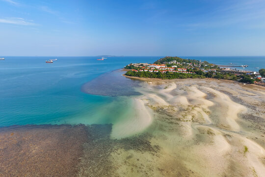 An expansive aerial panorama captures a vibrant coastal community, with numerous buildings nestled among green trees on a peninsula, bordered by blue ocean