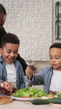 A diverse family happily prepares a healthy salad together in a bright, modern kitchen, learning to cook from a laptop
