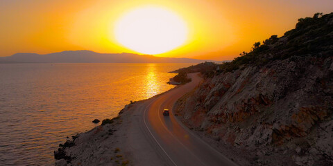Fototapeta premium AERIAL: Black SUV drives up a winding road with a perfect view of the calm ocean