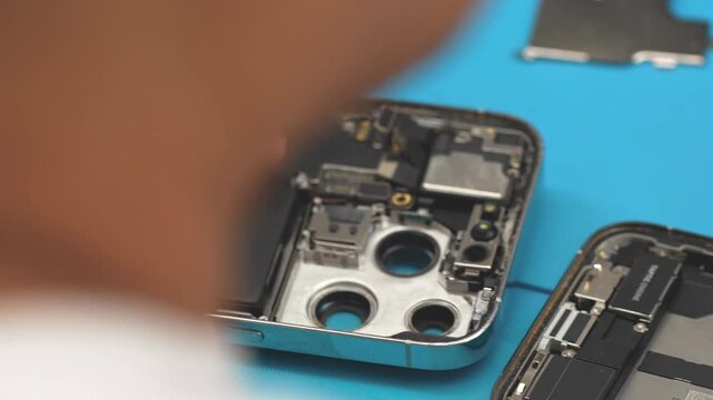 Technician repairing smartphone motherboard after disassembly in electronics repair workshop