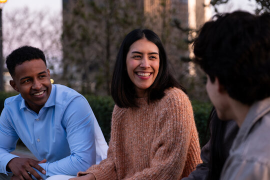 Diverse young adults are smiling, laughing, and talking together outdoors in a city setting