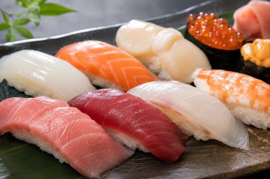 Premium nigiri sushi assortment on dark slate &mdash; tuna, salmon, scallop, shrimp, ikura, uni close-up overhead, Japanese omakase platter, high-end restaurant food photography
