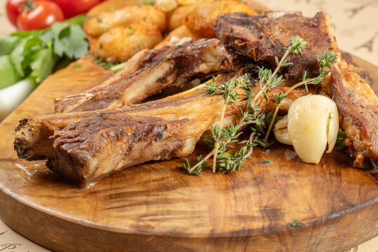 Close-up of grilled lamb chops with fresh thyme and roasted garlic served on a rustic wooden platter.