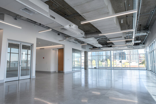 Expansive interior shot showcasing a modern, empty commercial space with polished concrete floors and large windows. The ceiling reveals exposed ductwork
