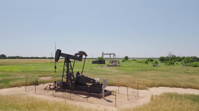 Drone 4K of a wheat field with two oil pump jacks and wind turbines in the background.