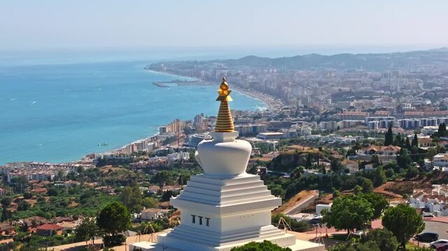 Drone footage approaching the Benalm&aacute;dena Stupa with the Costa del Sol, turquoise Mediterranean, and city sprawl stretching behind it under hazy summer light.