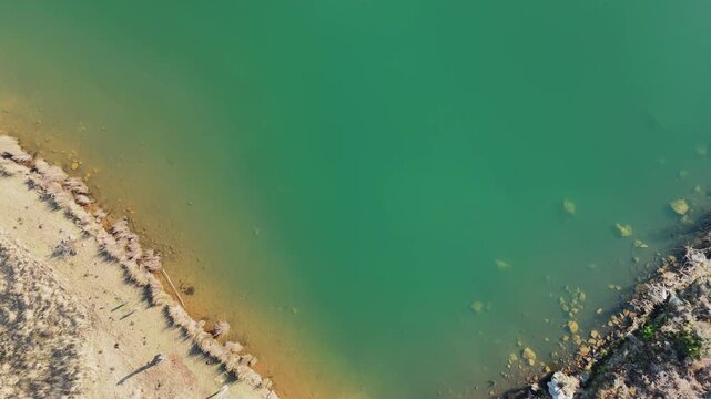 Top down drone shot revealing a heart-shaped turquoise lake with a small stone dam and wooden jetty in a rocky mountain landscape.