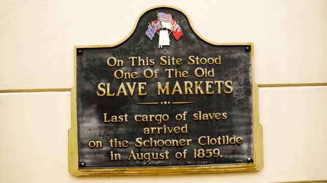 A tilt shot moves downward across a marker in Mobile, Alabama, referencing the schooner Clotilde, the final known illegal slave shipment brought into the United States.