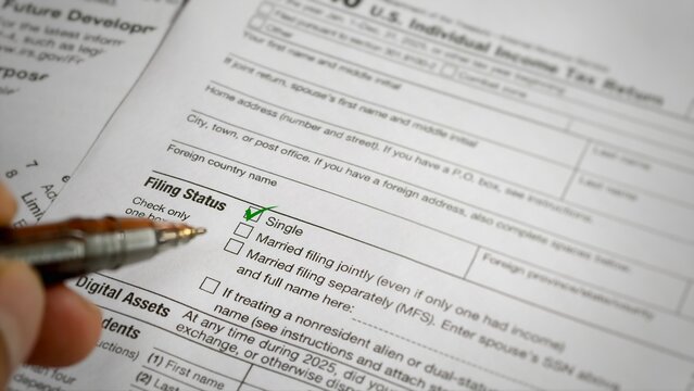 A close-up informational view of an IRS Form 1040 U.S. Individual Income Tax Return, showing a hand with a pen pointing to a green checkmark next to the "Single" filing status box.