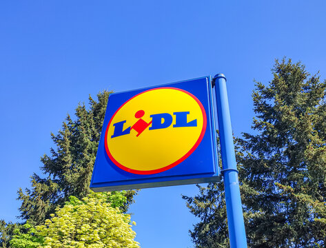 Le Mans, France - April 24, 2026: Lidl supermarket sign against clear blue sky with green trees in background, retail branding visible