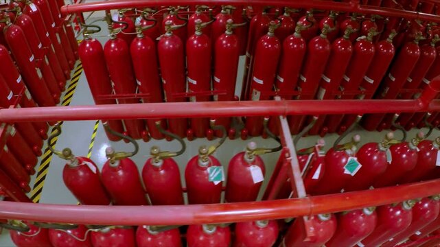 Rows of red fire suppression cylinders connected through industrial piping system inside organized safety and protection facility environment