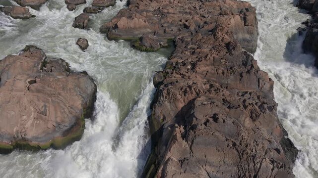Aerial shot flying backwards downstream in slow motion at a low height, showing the power and water flow at Khone Phapheng falls in Laos