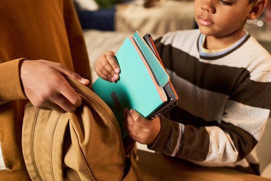 Black child packing notebooks into backpack with parent helping, preparing for school routine and learning. Education concept for back to school, parenting, childhood development