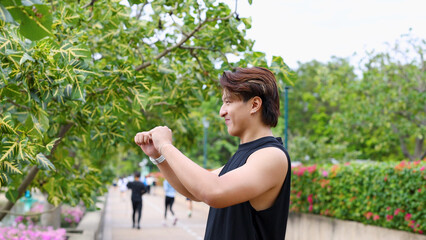 Fototapeta premium Asian Man in Black Sleeveless Shirt Stretching Arms in Lush City Park