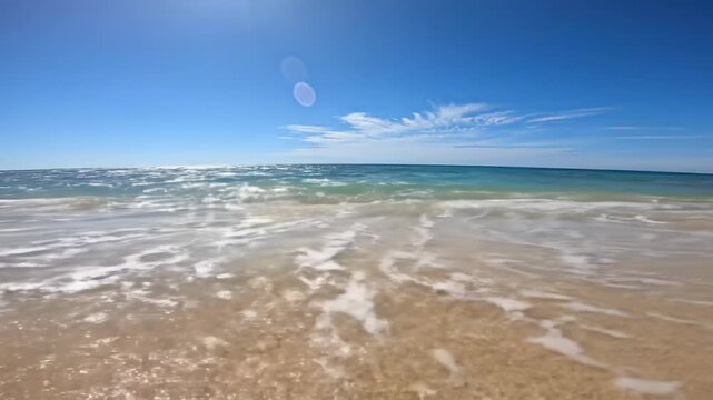 Wide video of a pristine golden sand beach, turquoise waves, cerulean ocean under an azure sky. Wet sand reflects light, fixed eye-level video captures tranquility. Tropical paradise ambiance