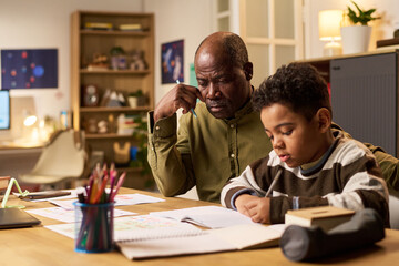 Fototapeta premium Black senior man assisting Black boy with homework at desk, supporting learning and family education at home. Useful for parenting, tutoring, homeschooling, child development campaigns