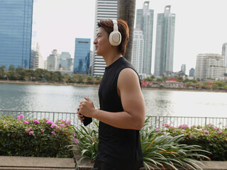 Obraz premium Asian Man Jogging in Benjakitti Park with Bangkok Skyline Background