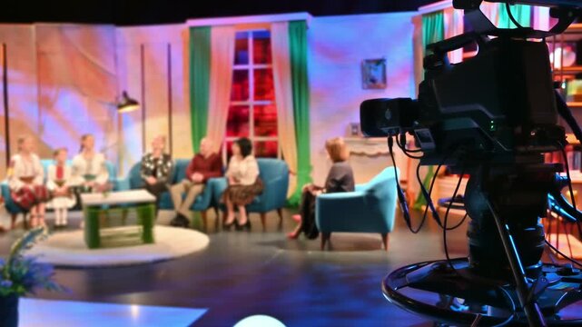 Television studio camera filming live talk show broadcast with blurred people on stage.