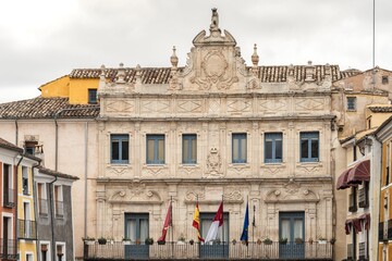Obraz premium Front view of the Baroque style Town Hall Ayuntamiento building with its characteristic stone arches blue windows and official flags in the Plaza Mayor of Cuenca Spain