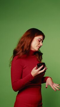 Happy young woman with red hair using a smartphone and earbuds on green screen background. Perfect for technology, communication, or lifestyle projects.