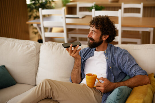 Bearded man recording voice memo relaxing on sofa