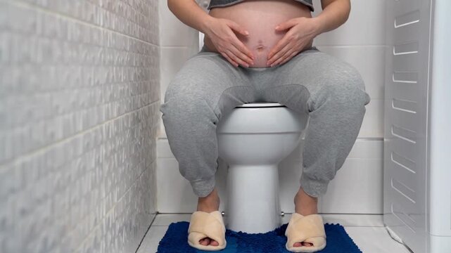 Pregnant woman sitting on toilet at home bathroom, illustrating frequent urination during pregnancy. Maternity health, prenatal symptoms, bladder pressure and pregnancy discomfort concept in everyday 
