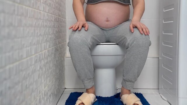 Pregnant woman sitting on toilet at home bathroom, illustrating frequent urination during pregnancy. Maternity health, prenatal symptoms, bladder pressure and pregnancy discomfort concept in everyday 