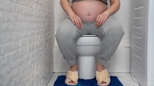 Pregnant woman sitting on toilet at home bathroom, illustrating frequent urination during pregnancy. Maternity health, prenatal symptoms, bladder pressure and pregnancy discomfort concept in everyday 