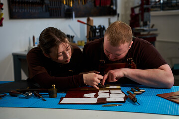 Fototapeta premium Leatherworkers in aprons working with cowhide and paper patterns.