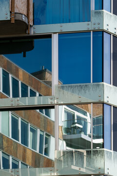 Balcony geometry frames a building facade where glass windows catch reflection across urban office architecture, emphasizing stacked detail and sharp edges