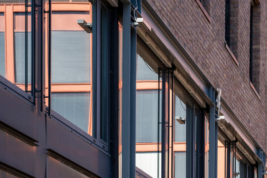 Warm light crosses a brick building facade as glass windows and reflection shape urban office architecture with repeating lines and narrow detail
