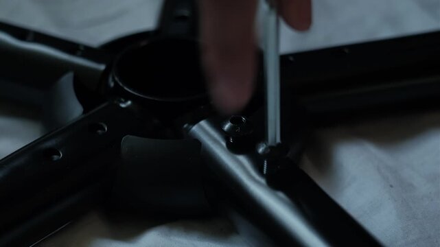 Close-up static shot of hands tightening a chair base with an allen wrench during furniture assembly indoors