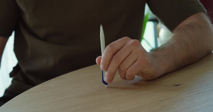 Person tapping a pen on a table, showing nervous behavior, stress, and restlessness in a casual setting.