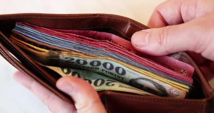 Man holds his open leather wallet filled with many hungarian forint banknotes and choosing the highest denomination of 20000.