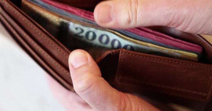 A hand holds an open brown leather wallet filled with many hungarian forint banknotes in there including a visible denomination of 20000 bill.