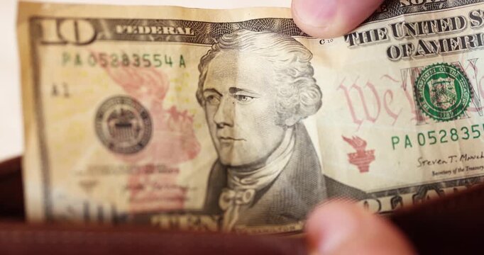 Quickly moment of checking a ten-dollar banknote while is in the brown leather wallet for daily spending.