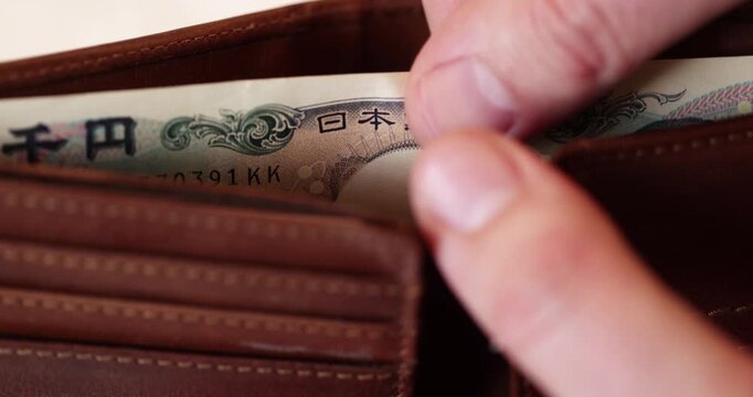Close-up showing perspective shot of thousand japanese yen banknote stored inside a brown leather wallet like the only bill in the purse.