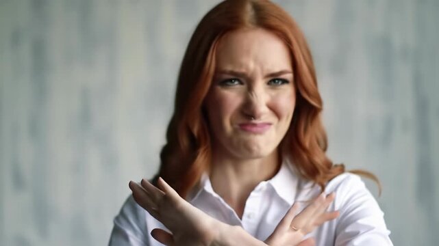 Young caucasian woman with auburn hair, green eyes, white button-up shirt expresses playful, firm rejection with 'stop' gesture against light gray studio wall, evolving emotions concept